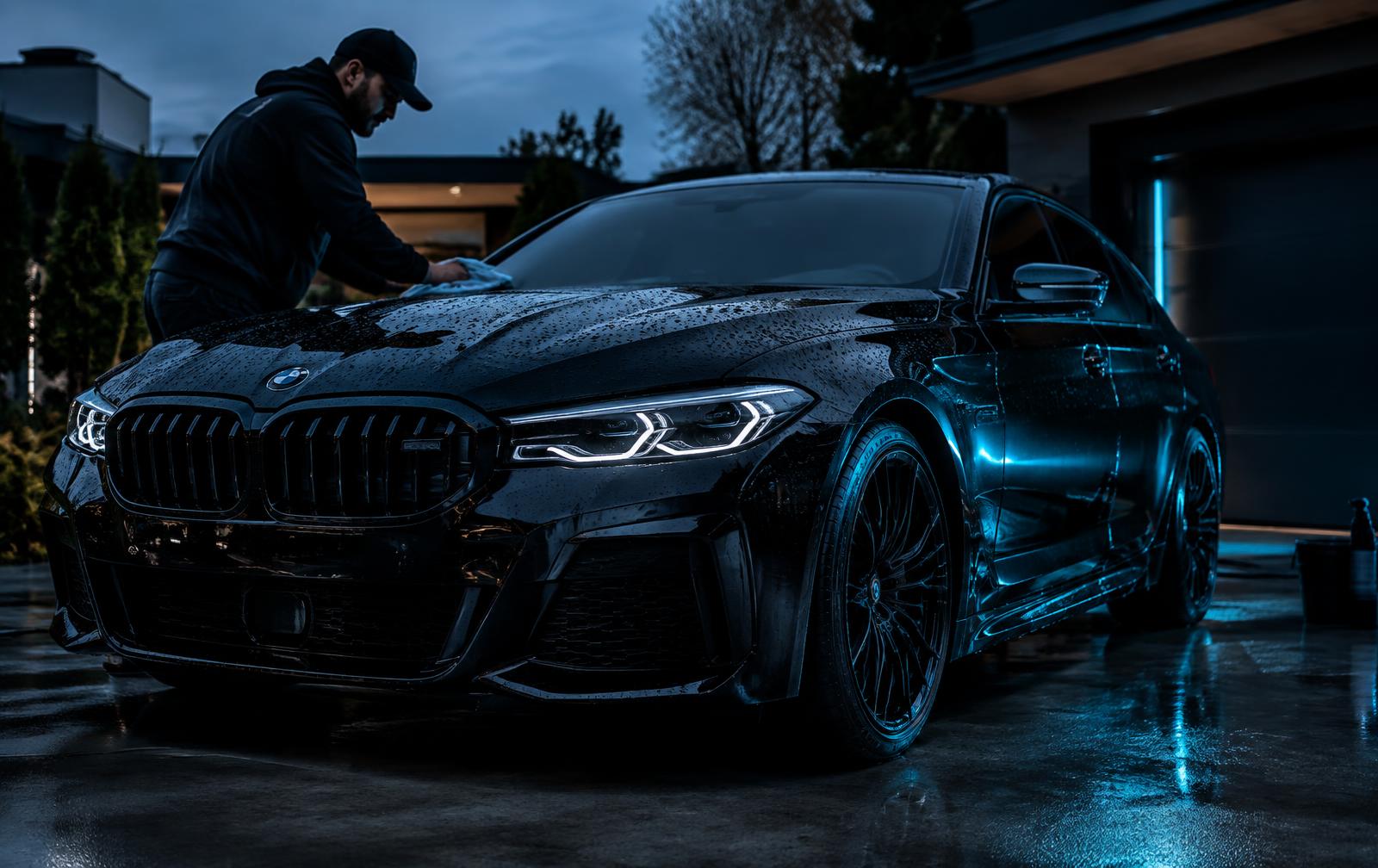 Detailer polishing a glossy black car in a driveway at dusk